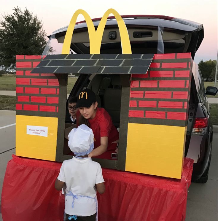 two children standing in front of a fake mcdonald's car with the back door open