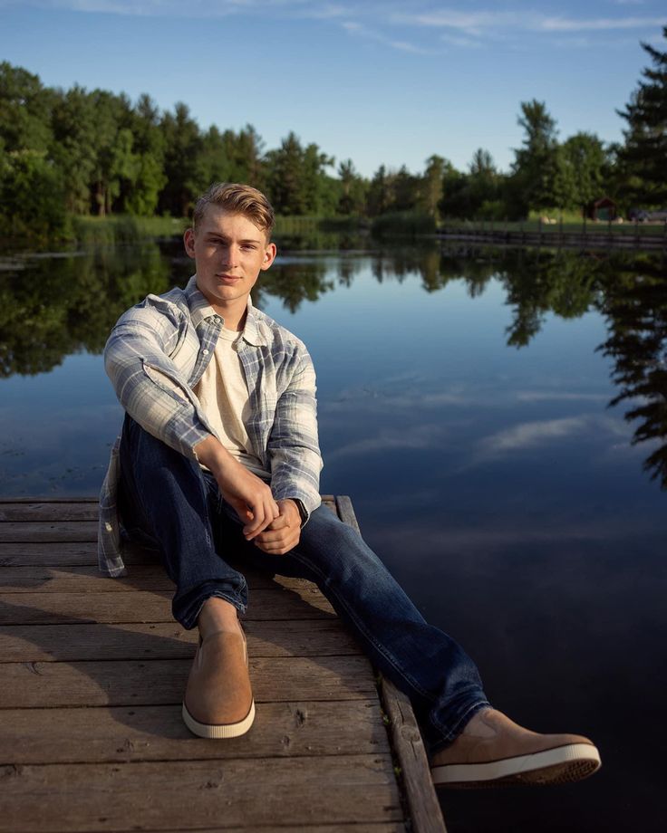 a man is sitting on a dock by the water with his legs crossed and looking at the camera