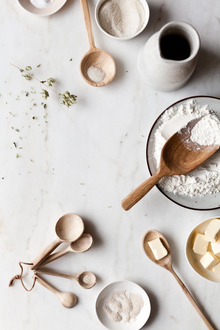 various wooden spoons and bowls filled with flour on a white counter top next to measuring spoons