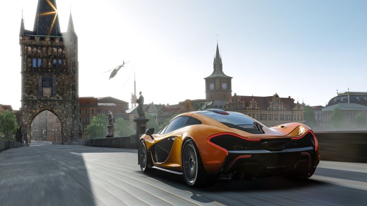 an orange sports car driving down a road next to a castle and clock tower in need of speed