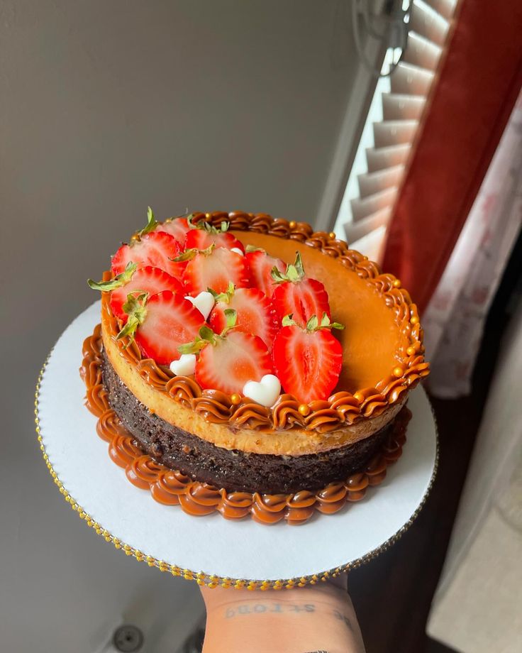 a hand holding a cake with strawberries on top