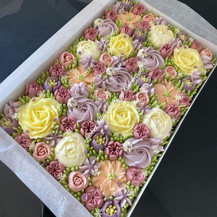 a box filled with lots of different colored frosting flowers on top of a table