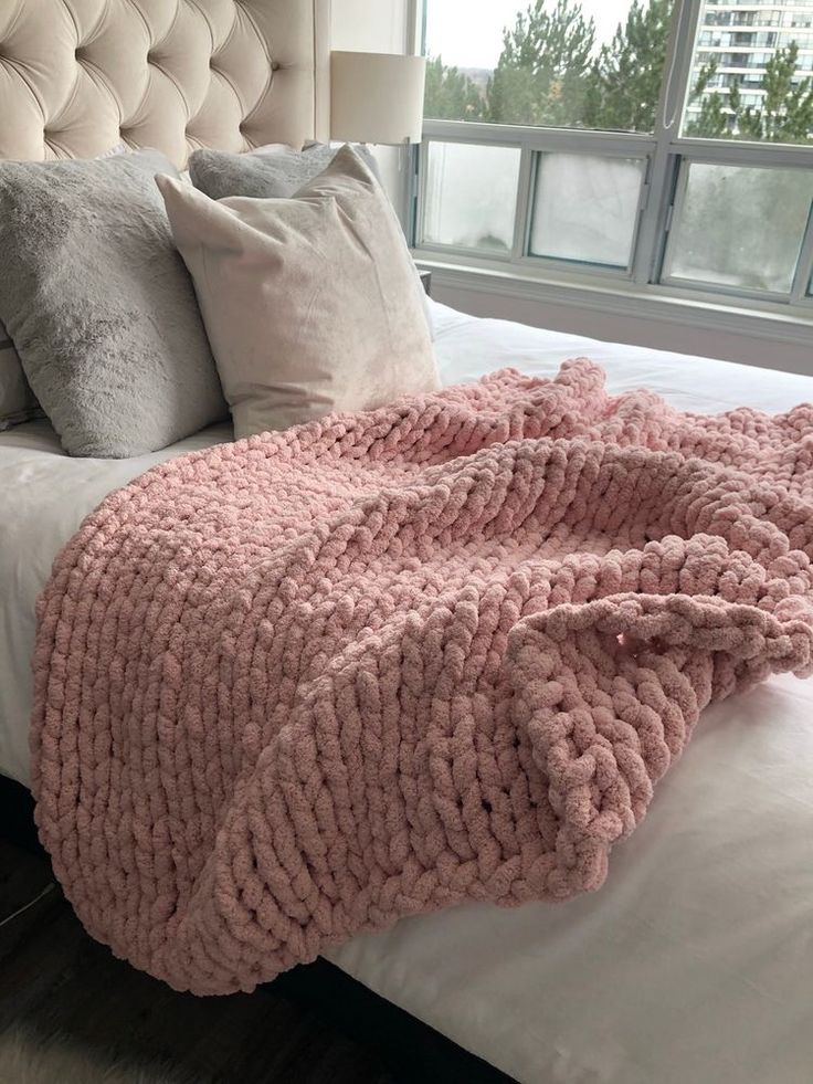 a large pink blanket on top of a bed next to two pillows and a lamp