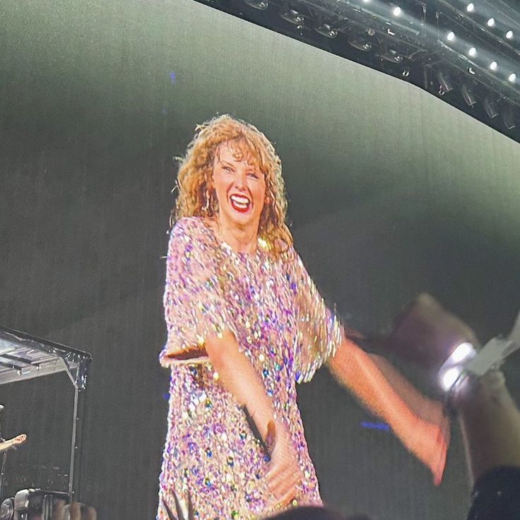 a woman is singing on stage with her arms out to the side as she stands in front of an audience