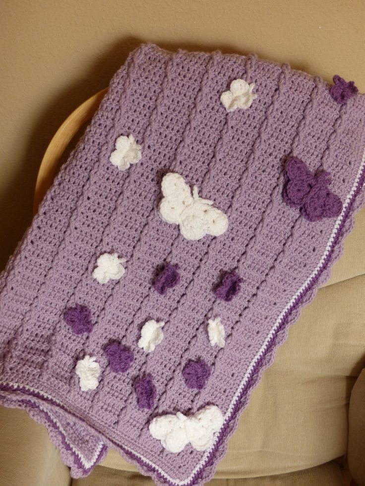 a purple crocheted blanket with white and purple flowers on it sitting on a chair