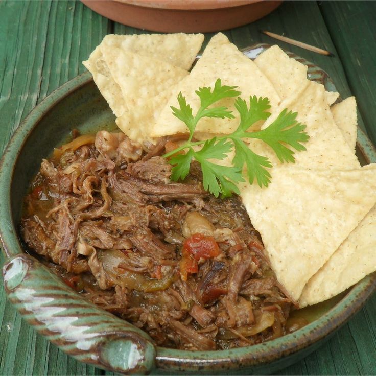 a bowl filled with meat and tortilla chips on top of a wooden table