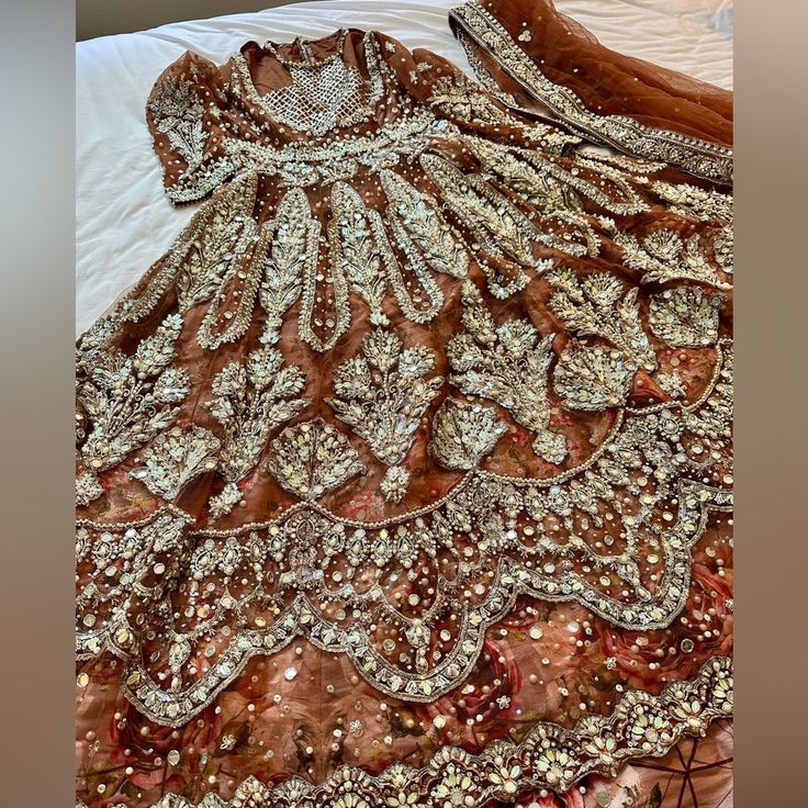 Hi I Am Selling A Beautiful Brand New Designer Suit From Saira Rizwan Based On Mm Alam Road It Is In Terra Cotta Red Brown Color, It Has Upper Gown With Lining, Printed Lengha And 4 Side Border Duppata. It Is Perfect For Any Special Occasion. Inside Lengha And Upper Gown Have 1-2 Inches Of Margin For Alterations. Measurements: Gown: Shoulder: 15 Inches Bust: 21 Inches Waist: 19 Inches Hips: 23 Inches Arm Hole: 16 Inches Bicep: 14 Inches Sleeve Length: 19 Inches Shirt Length: 53 Inches Trouser Me Festive Glamorous Lehenga With Dabka Work, Glamorous Dabka Work Lehenga For Festive Occasions, Glamorous Lehenga With Dabka Work For Festive Occasions, Glamorous Dabka Work Lehenga For Reception, Glamorous Festive Lehenga With Dabka Work, Luxury Embellished Lehenga For Wedding, Traditional Silver Hand Embellished Dress, Traditional Hand Embellished Silver Dress, Silver Dupatta With Dabka Work For Party