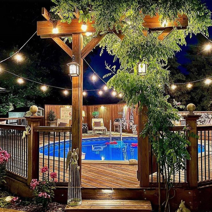 an outdoor pool with lights strung around it and a wooden gazebo surrounded by greenery