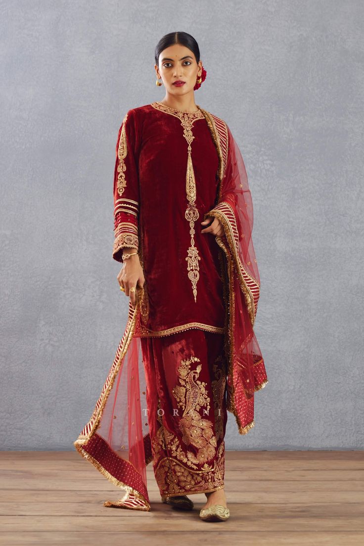 Editor's Note Featuring a bright red hand embroidered phiran set in silk velvet and embroidered sheer dupatta having sequin worked border Color: Red Fabric: Silk organza, silk velvet, cotton voile Components: Kurta, pant and dupatta Embroidery details: Hand embroidery, dori and hand adda work Fit: Loose Occasion: Wedding Guest Care: Dry Clean Only About the Designer Torani by Karan Torani stands handcrafted luxury inspired by the myriad tales of Indian mythology. Torani is a potpourri of all thi Luxury Raw Silk Dabka Embroidered Sets, Luxury Art Silk Salwar Kameez With Zari Work, Luxury Art Silk Churidar With Dori Work, Luxury Katan Silk Unstitched Suit For Puja, Luxury Dola Silk Salwar Kameez With Cutdana, Luxury Red Churidar With Cutdana Details, Luxury Red Unstitched Salwar Kameez, Luxury Red Georgette Unstitched Suit, Luxury Red Slub Silk Churidar