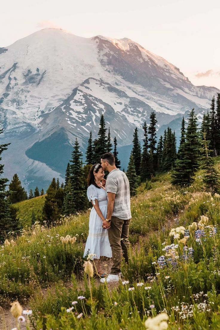 a man and woman standing on top of a lush green field next to a mountain