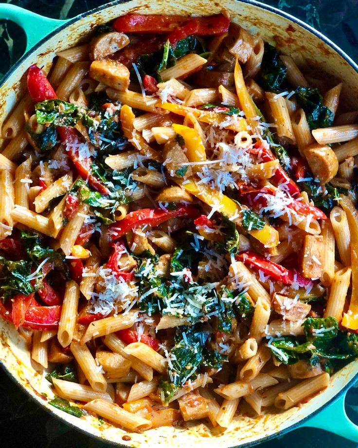 a pan filled with pasta and vegetables on top of a blue stovetop next to utensils