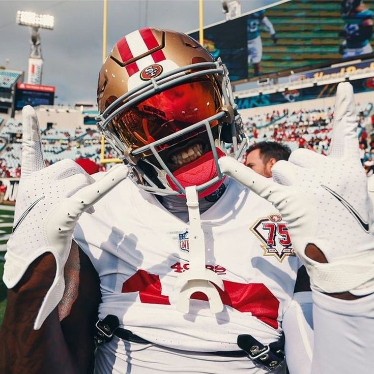 a football player wearing a helmet and holding his hands up in the air while standing on a field