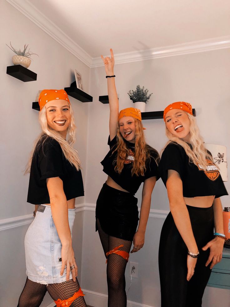 three women in black shirts and orange headbands posing for the camera with their hands up