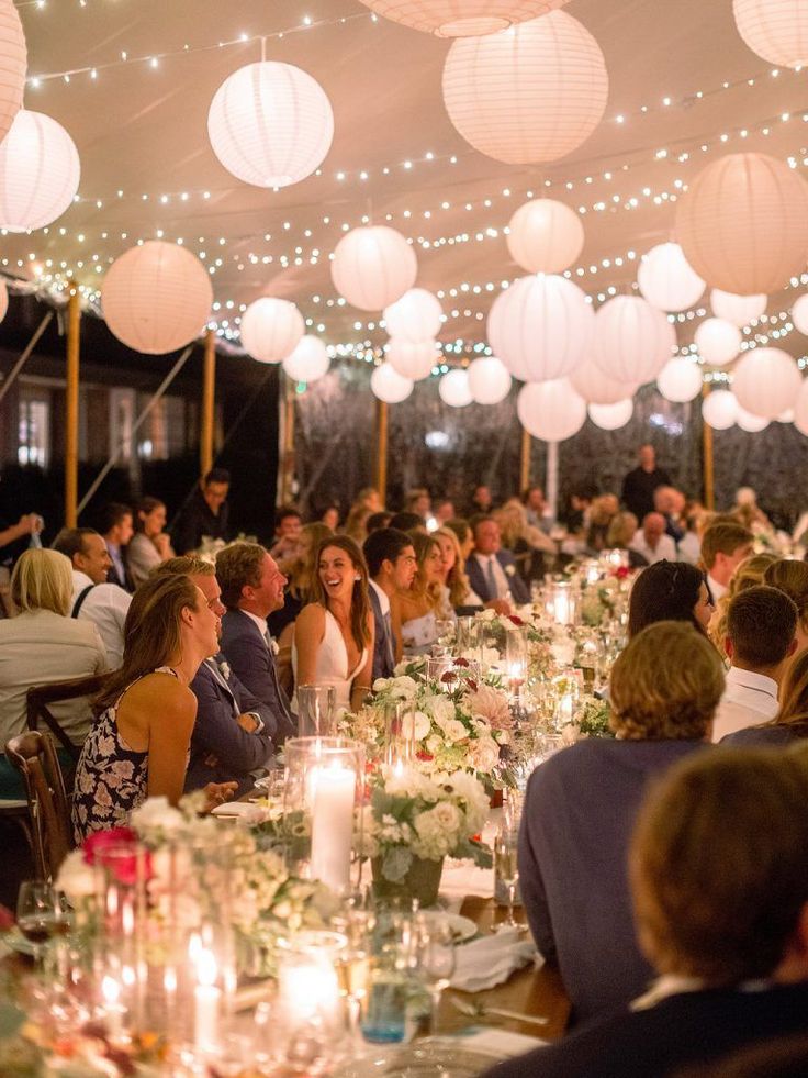 a group of people sitting at tables with paper lanterns hanging from the ceiling