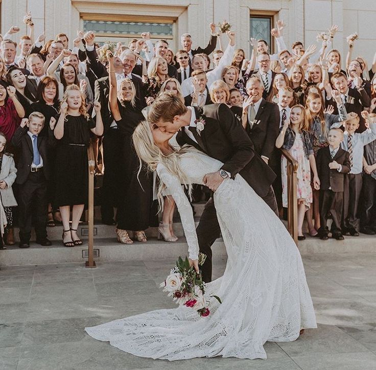 a bride and groom kissing in front of a large group of people holding their hands up