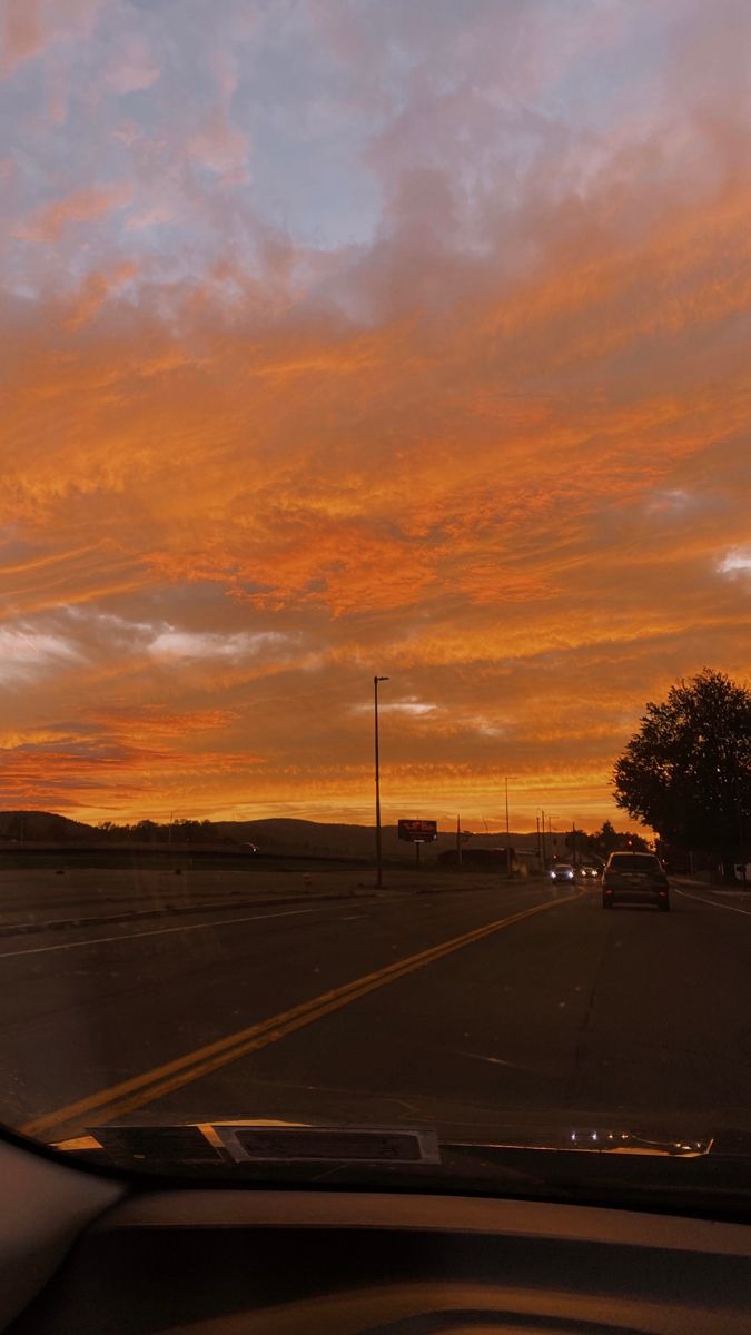 the sun is setting over an empty road with cars driving down it and trees in the distance