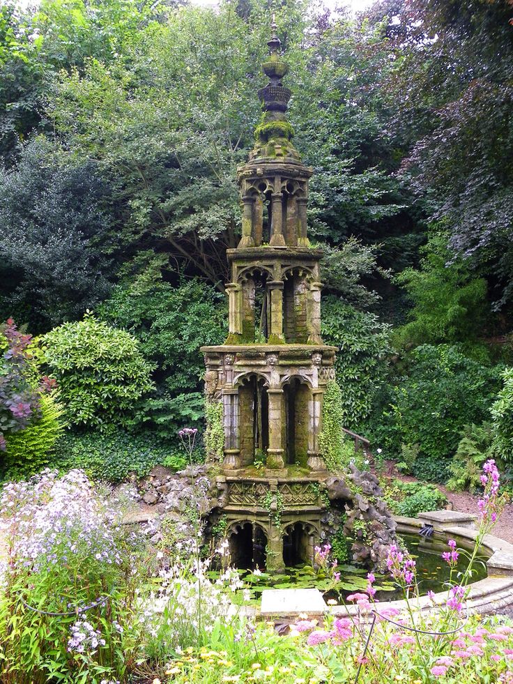 an old water fountain surrounded by flowers and trees