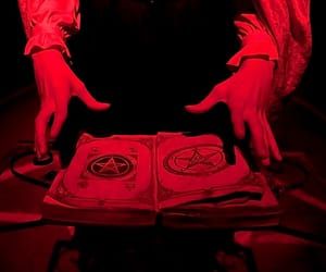 two hands reaching for an open book with pentagram written on it in red light