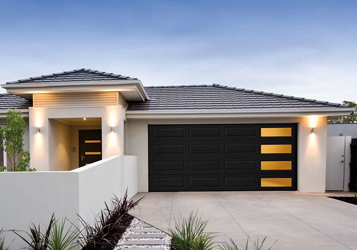 a white house with black garage doors and lights on the side of it's windows