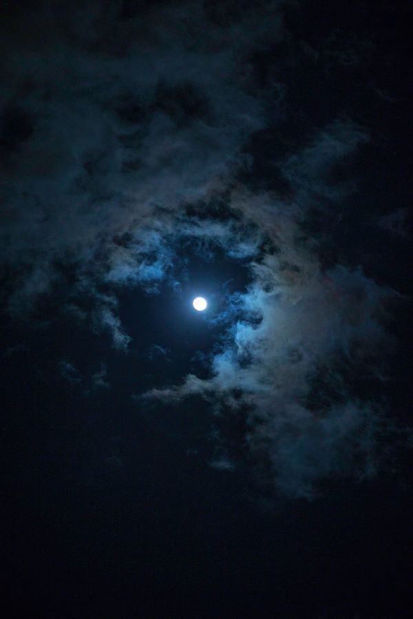 the moon is shining brightly in the night sky with clouds and dark blue hues