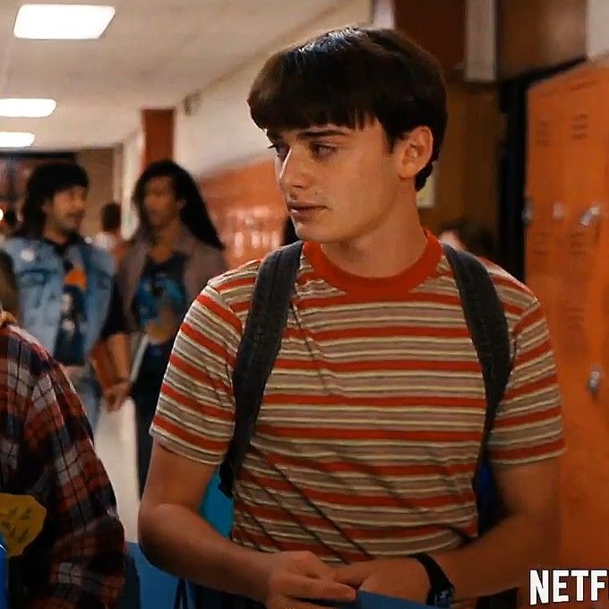 two young men standing next to each other in a hallway with lockers behind them