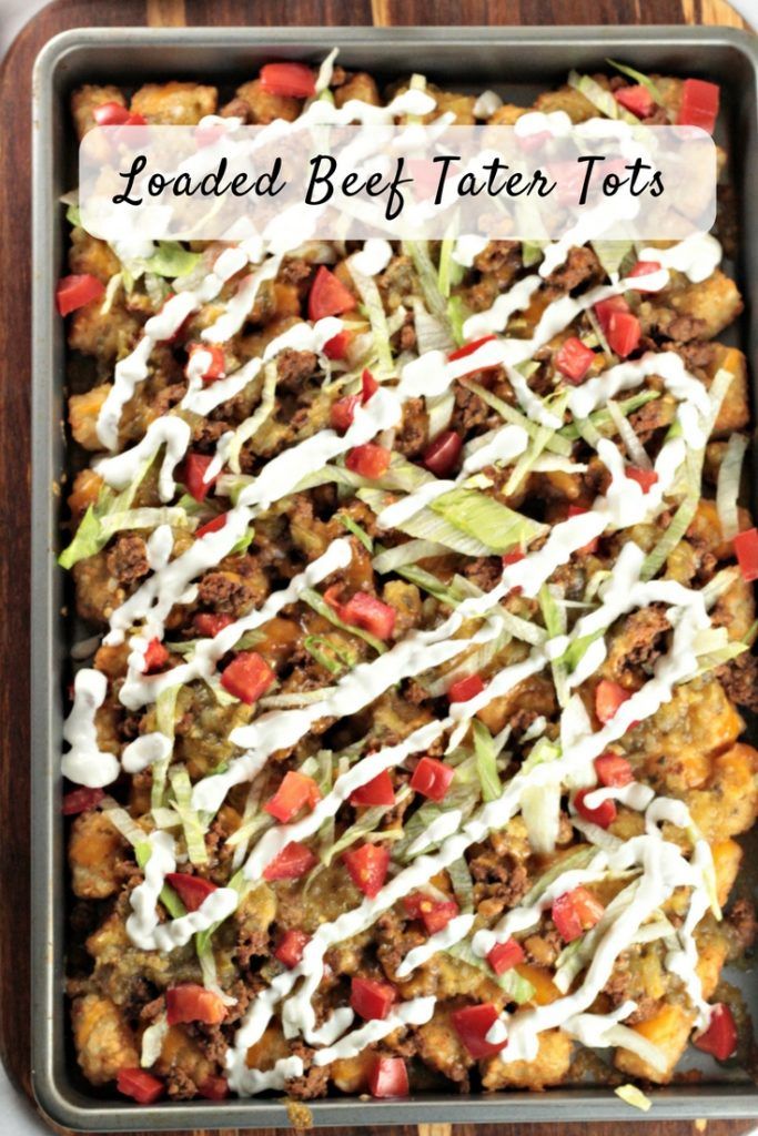 loaded beef tater tots in a baking pan with white sauce drizzled on top