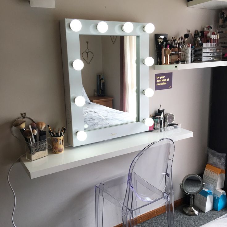 a vanity mirror sitting on top of a white shelf next to a chair and desk