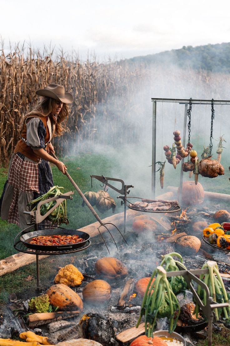 a woman cooking food on top of a grill next to corn stalks and pumpkins