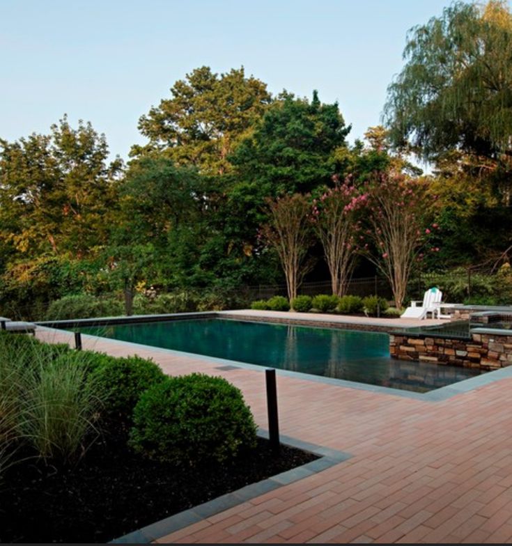 an empty pool surrounded by trees and shrubs in the middle of a garden area with brick pavers