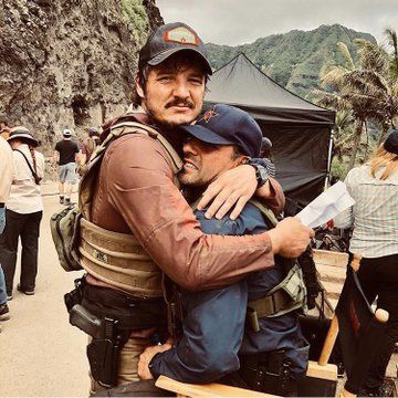 two men hugging each other while standing in front of a mountain with people around them