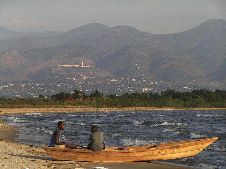 two people sitting in a small boat on the beach with mountains in the back ground