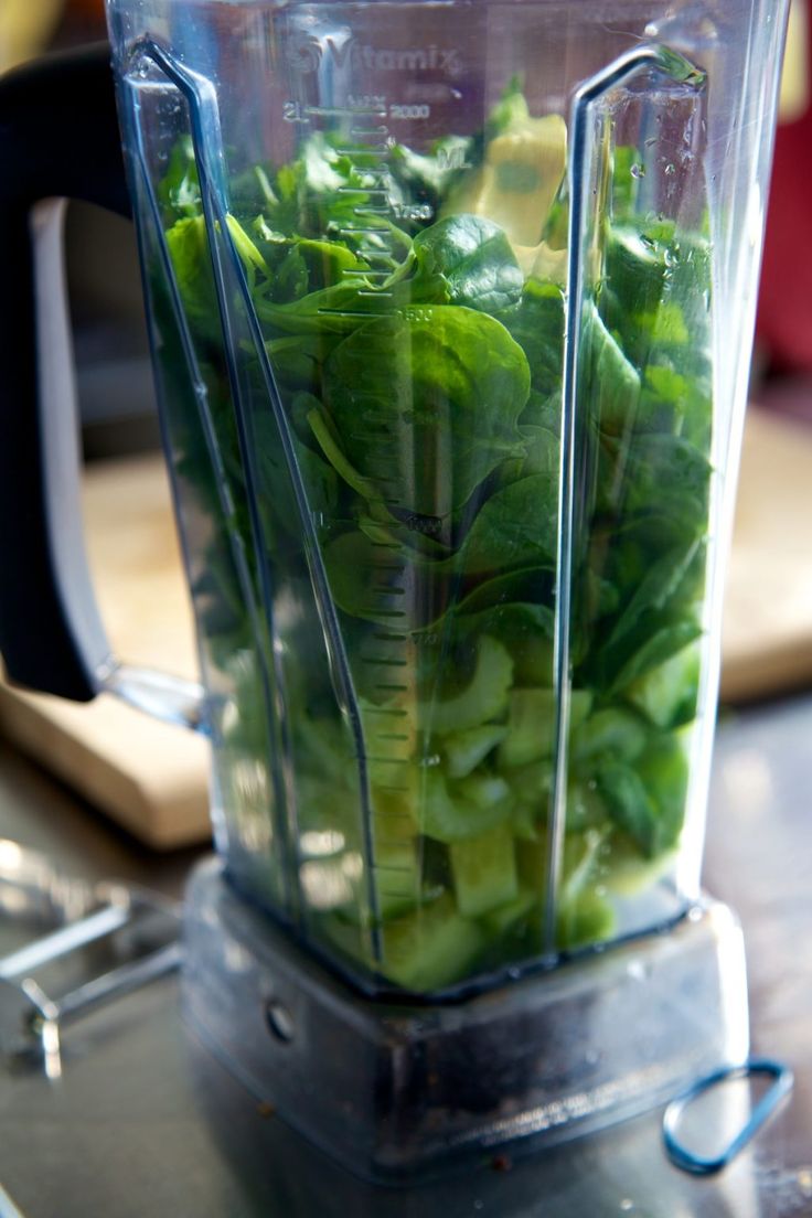 a blender filled with green vegetables on top of a table