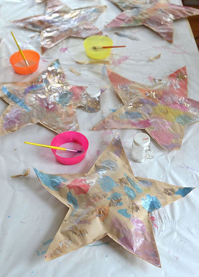 some paper stars are sitting on a table with paint and crafting supplies around them