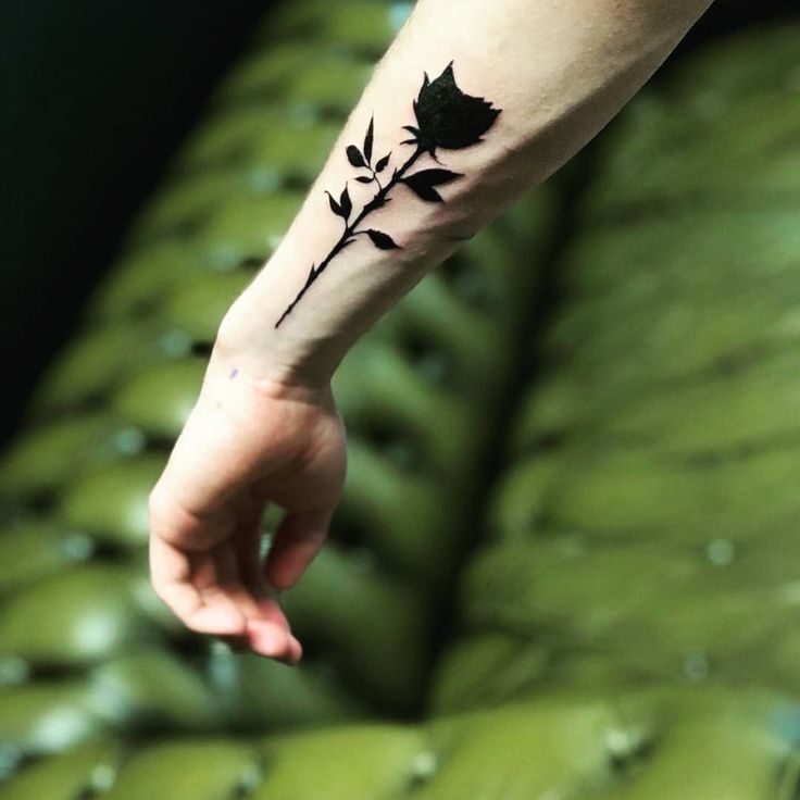 a small black rose tattoo on the left inner arm and wrist, with leaves coming out of it