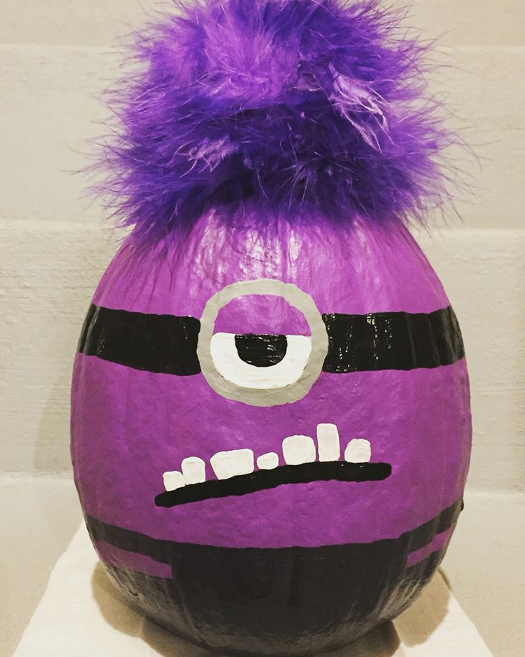 a purple and black painted pumpkin with a fuzzy ball on it's head, sitting on a white surface