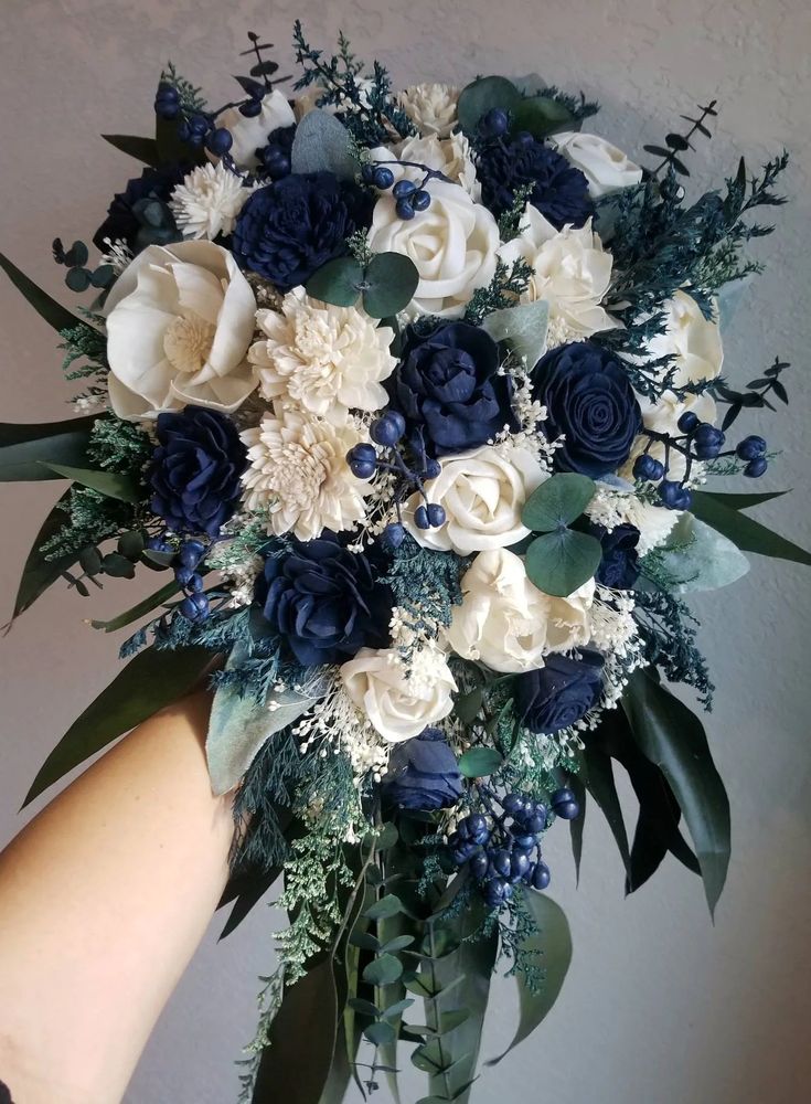 a bridal bouquet with blue and white flowers in someone's hand against a wall