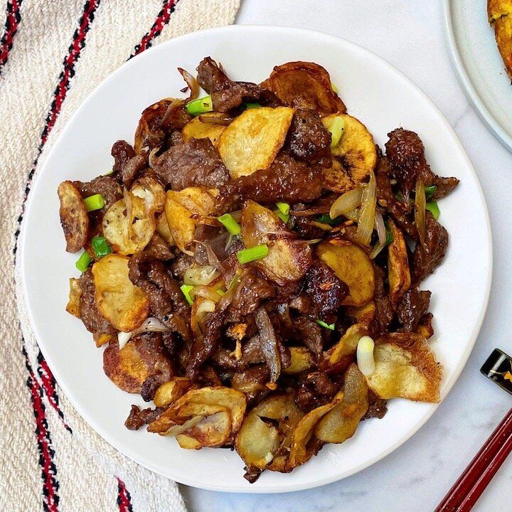 a white plate topped with meat and potatoes next to chopsticks on a table