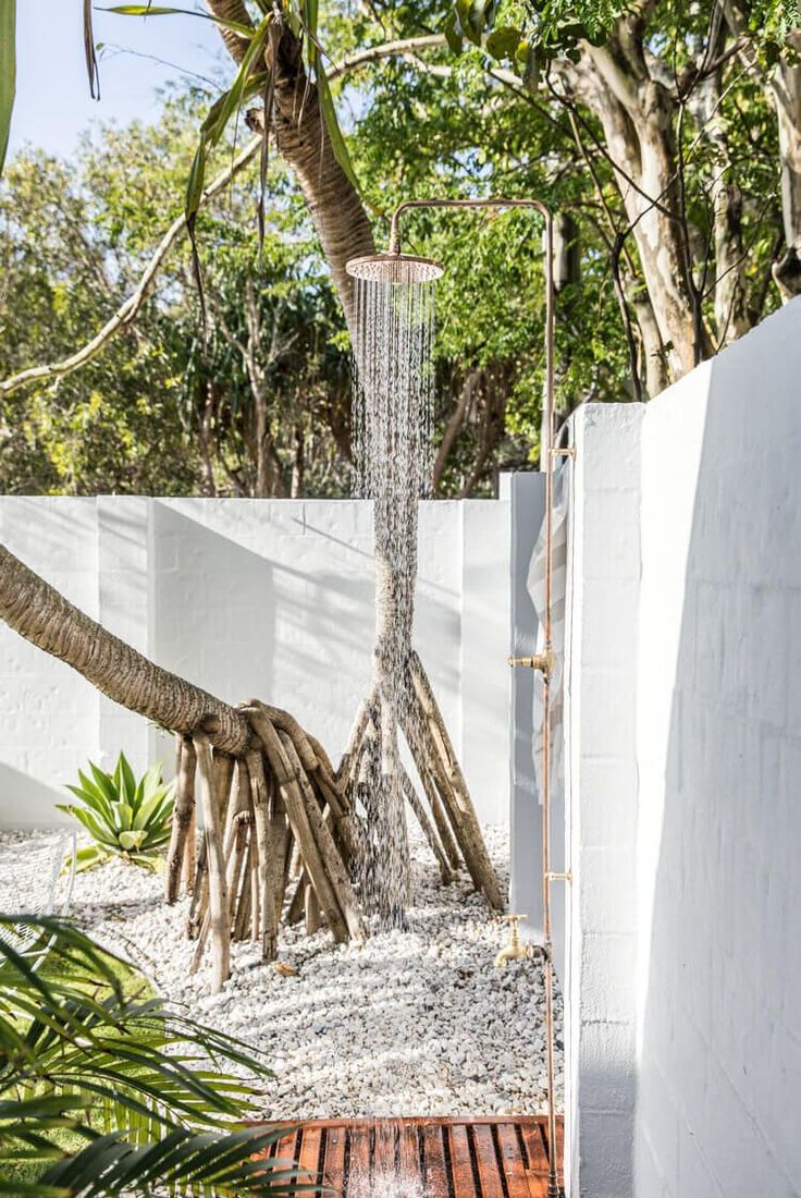 an outdoor shower in the middle of a wooden deck next to a white wall and trees