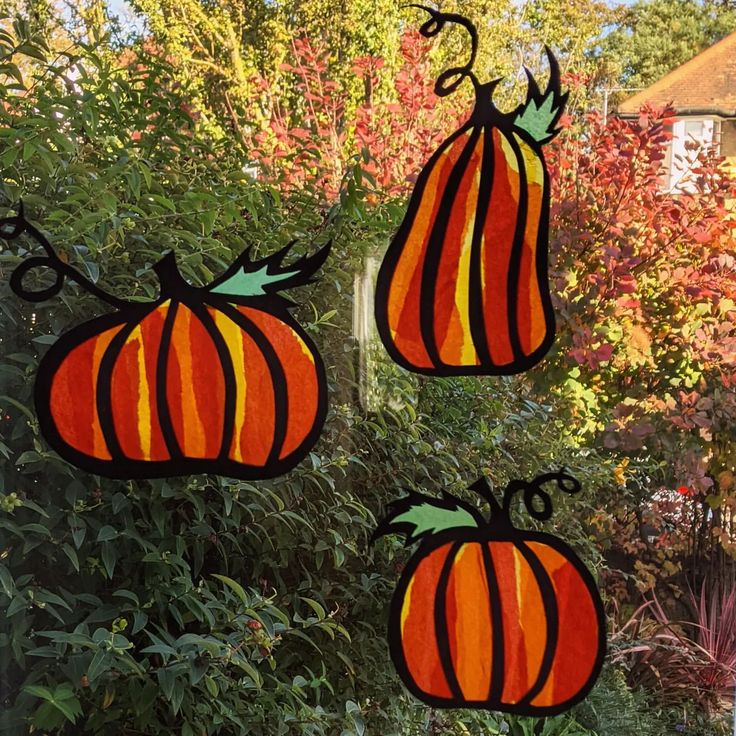 three pumpkins are hanging from a window in front of some bushes and trees with red leaves