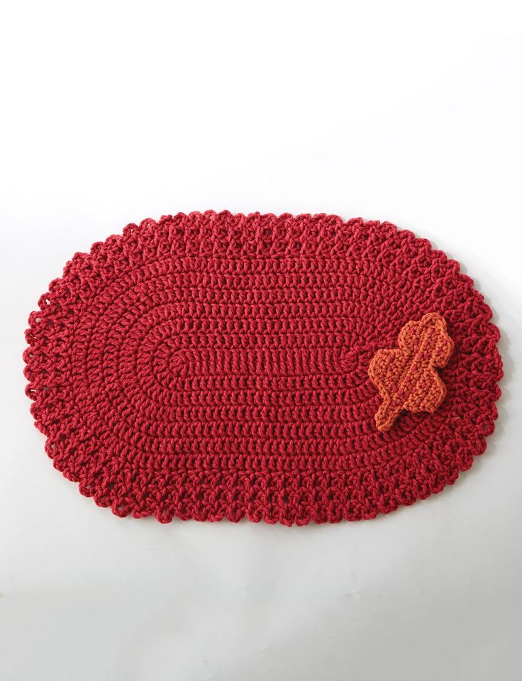 a red crocheted placemat with an orange flower on the center and a brown button in the middle