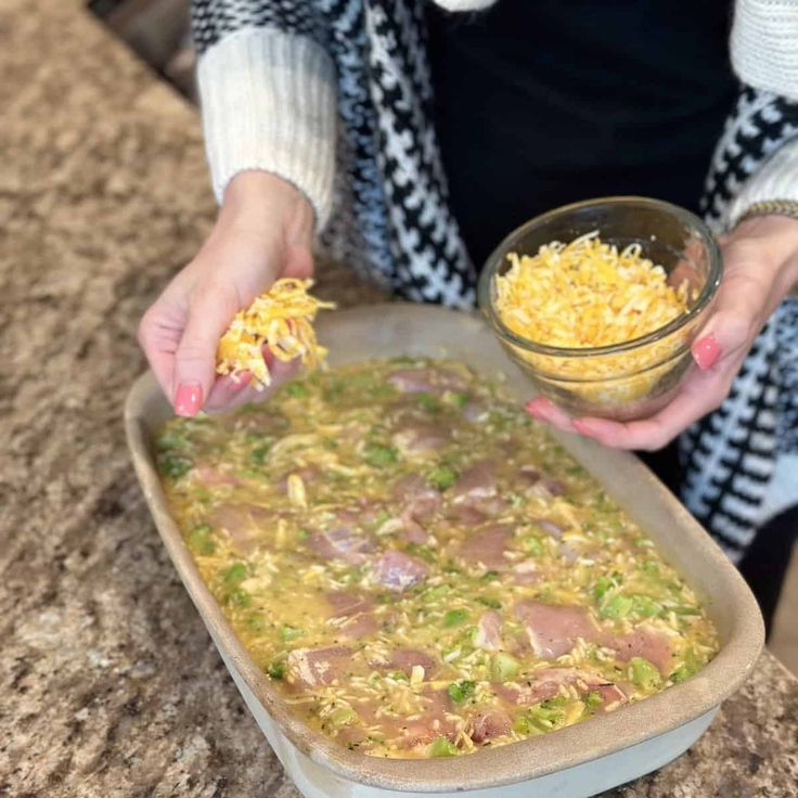 a woman holding a bowl filled with food on top of a counter next to a pan