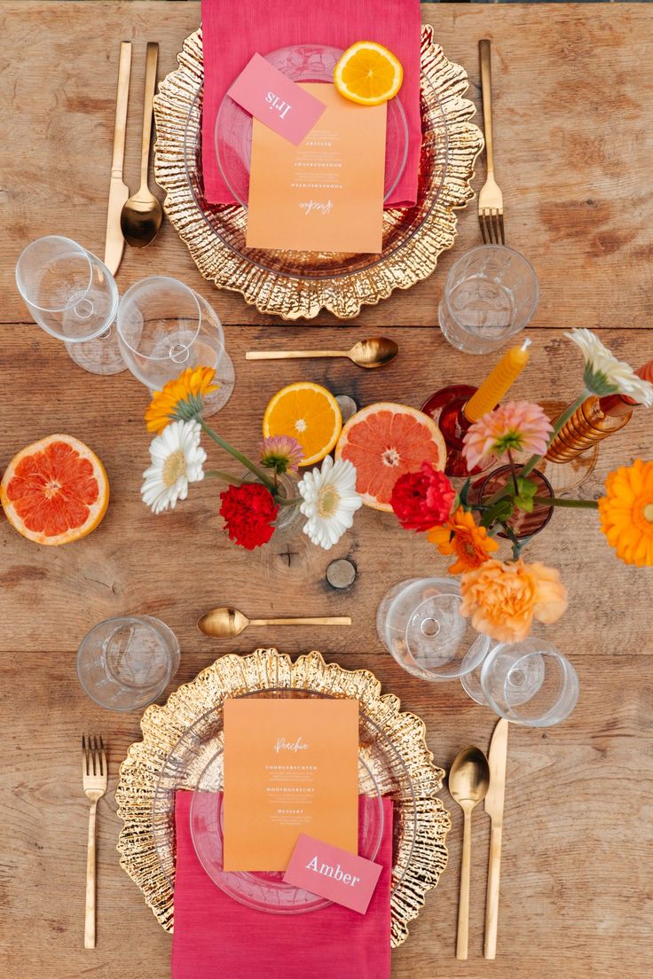 the table is set with oranges, pink napkins and gold chargerserware