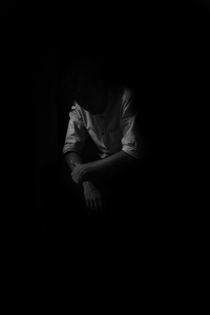 a man sitting in the dark with his arms folded over his chest and hands on his knees