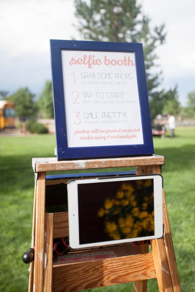 an ipad sitting on top of a wooden stand in front of a sign that says selfie booth