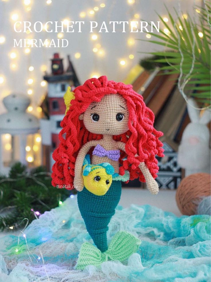 a crochet mermaid doll sitting on top of a blue blanket with lights in the background