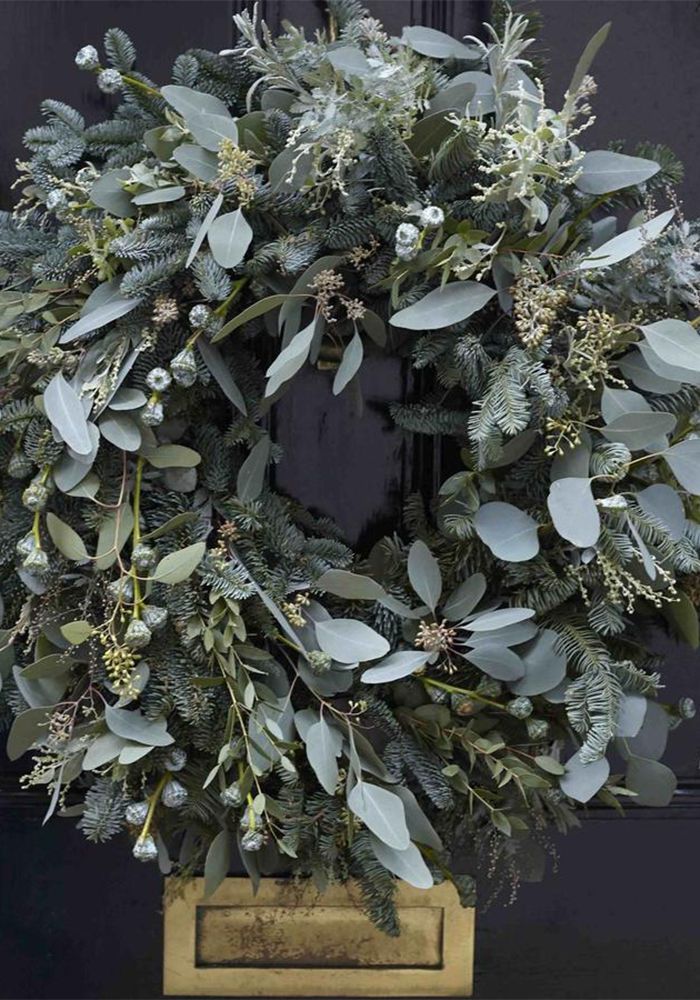 a wreath on the front door with green leaves and greenery hanging from it's sides