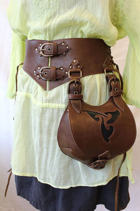 a woman wearing a brown leather purse with chains and buckles on her belt is standing in front of a white background