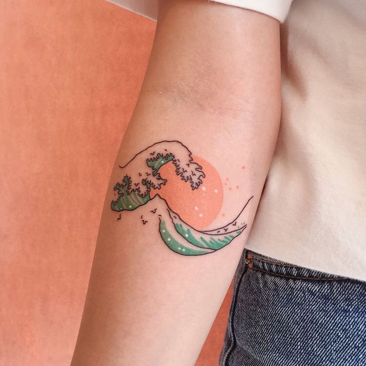 a woman's arm with a tattoo on it that has an image of a wave coming out of the water