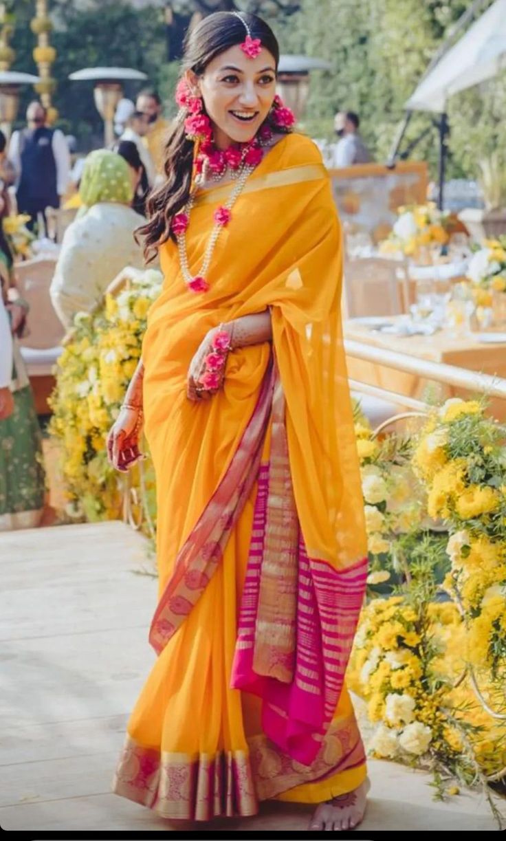 a woman in an orange and pink sari posing for the camera with flowers around her