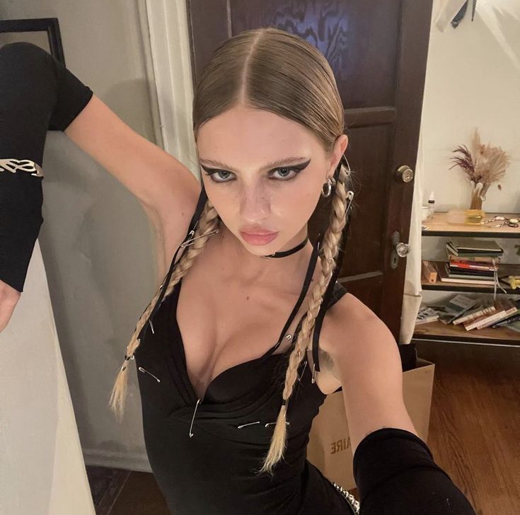 a woman with long braids in a black dress is posing for the camera while holding her arm behind her back